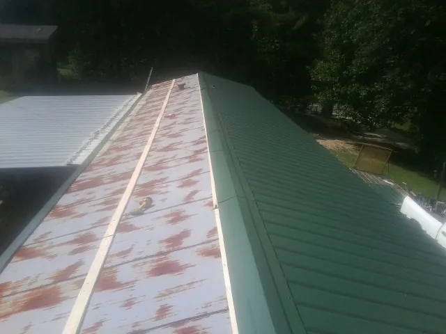 Old rusted panels beside newly installed green metal roofing — Wind Damage Roof Repair by Roofing Brothers in Church View