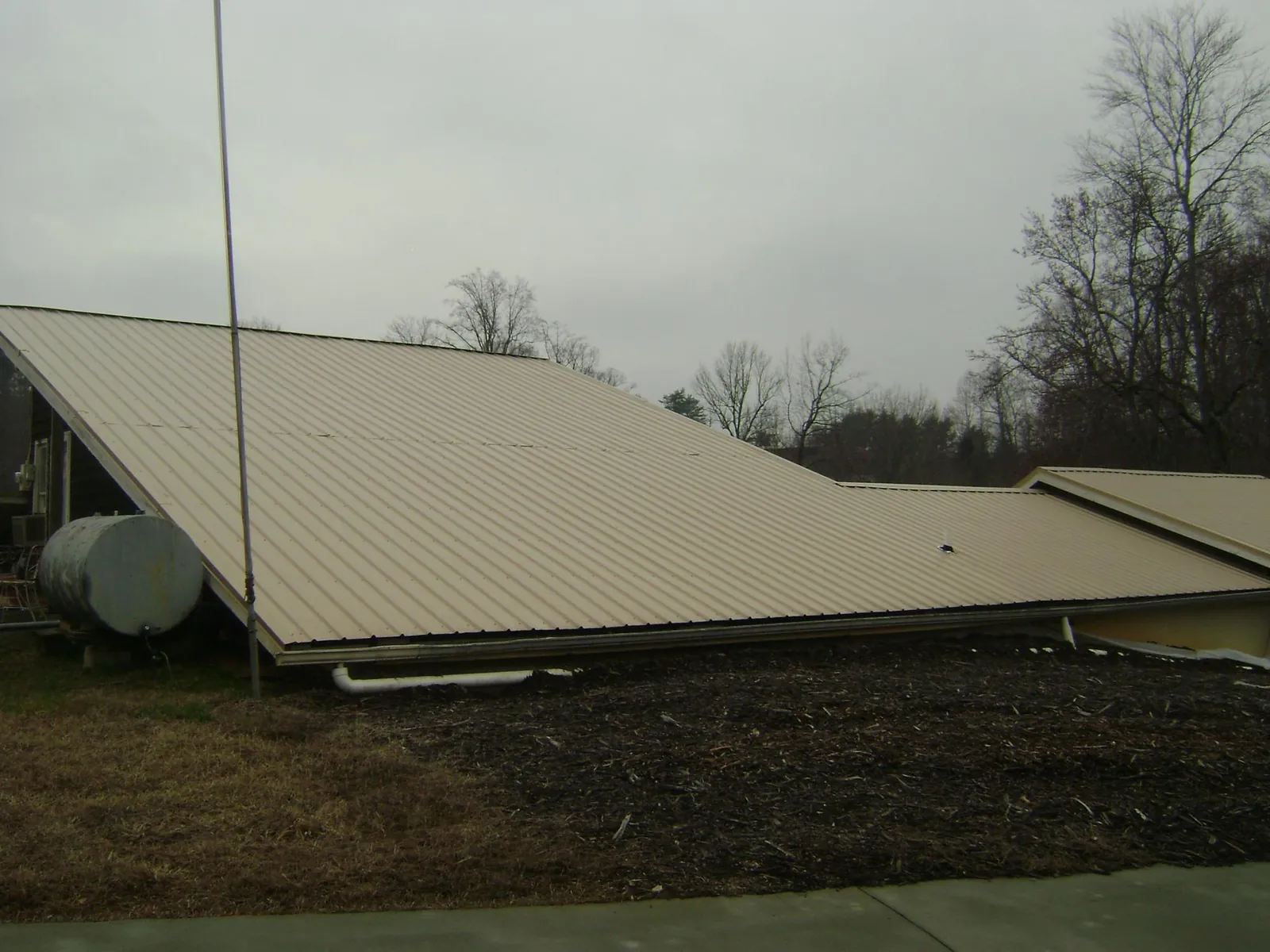 Wide tan metal roof plane seen from the ground beside a propane tank in Church View