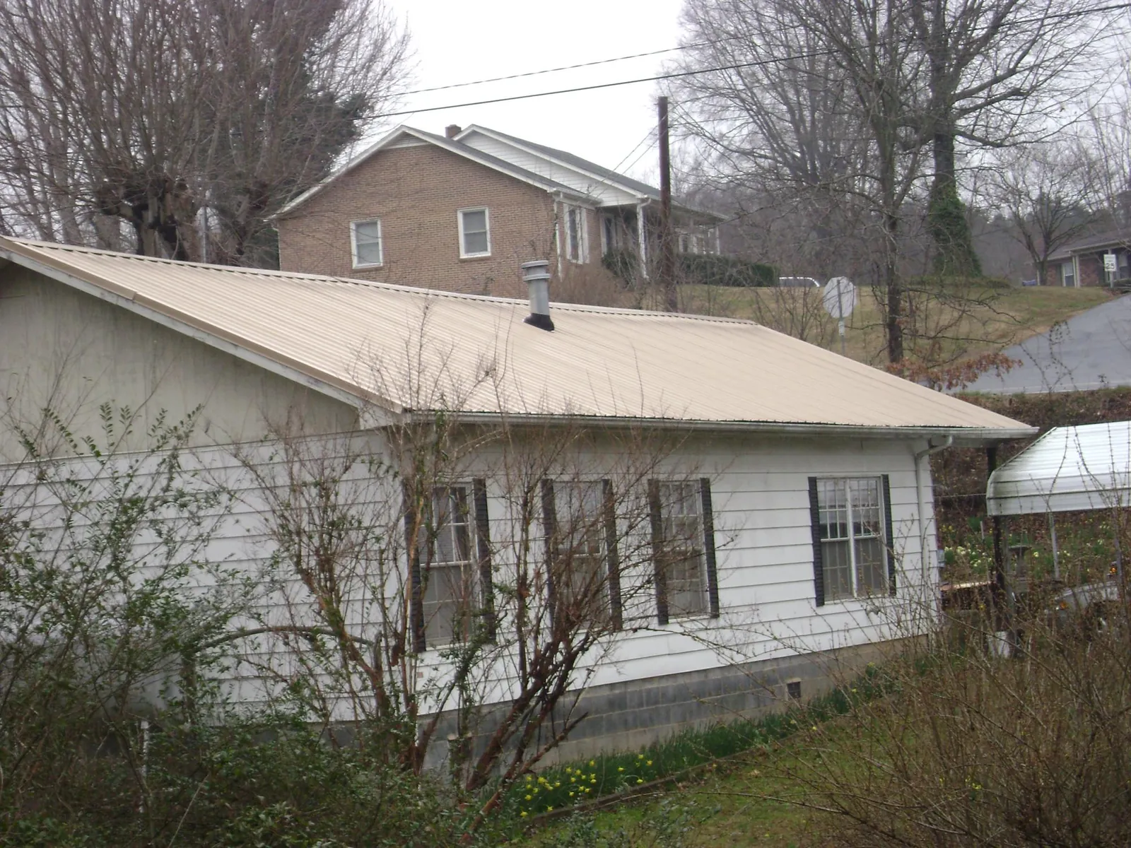 Tan metal roof on a white sided house set into a hillside — Commercial Roofing by Roofing Brothers in Church View